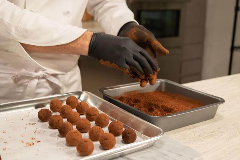 Chef with gloves on making chocolate truffles in a kitchen