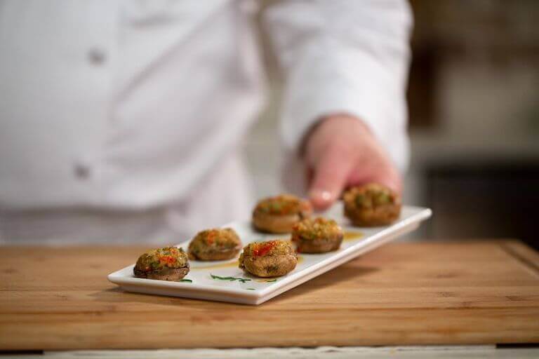 Close up image of a chef holding a white plate full of stuffed mushrooms