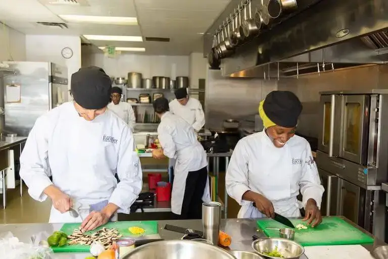 Culinary students practice knife skills and food preparation together in a professional teaching kitchen at Escoffier’s Boulder campus.