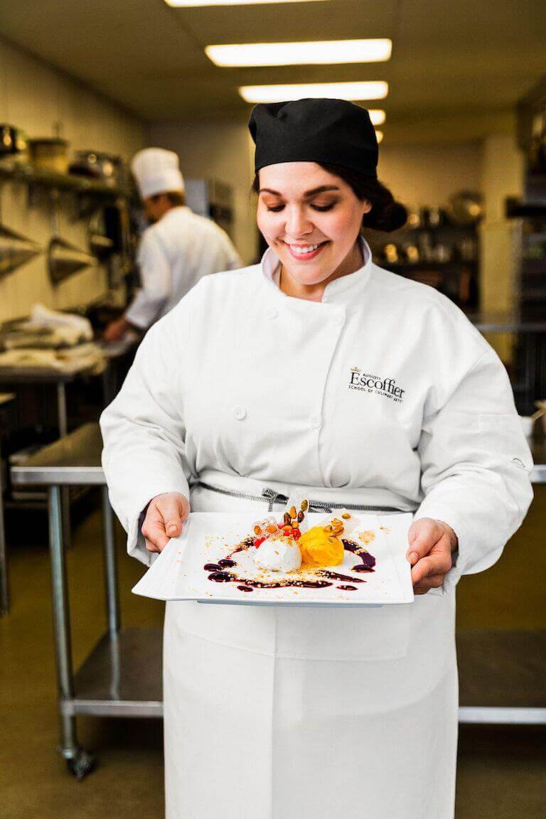 Escoffier student holding a plated dessert in the kitchen