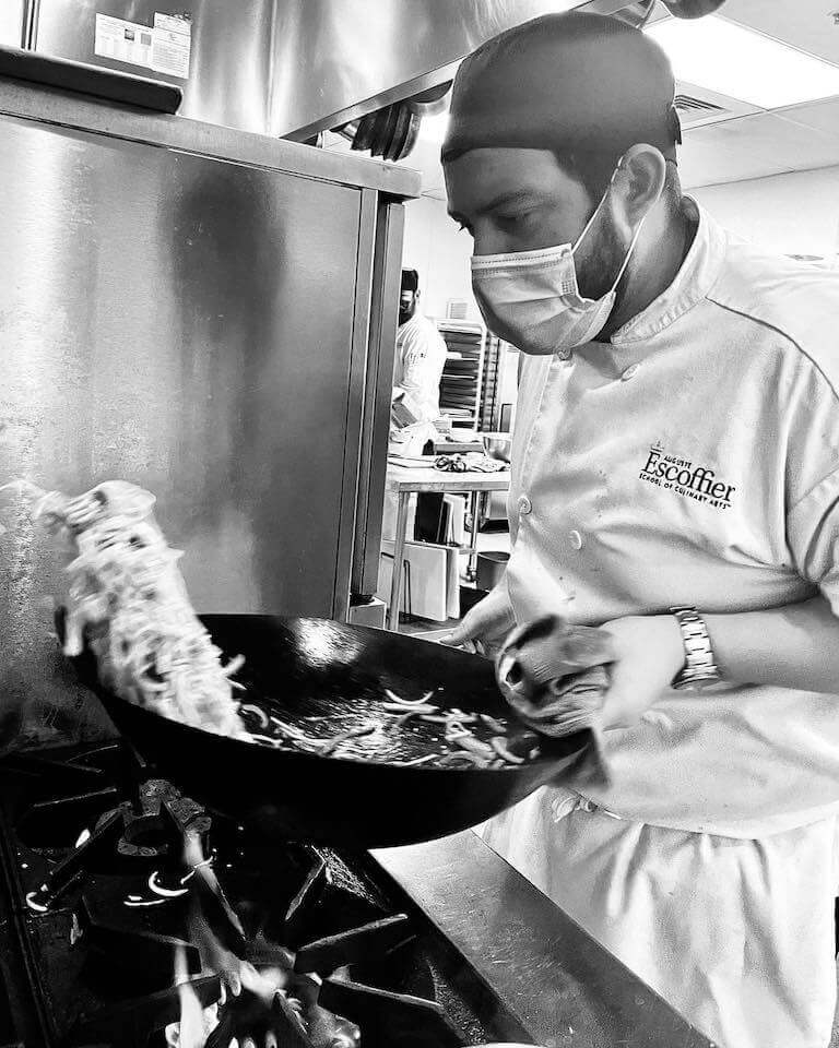 Escoffier student stirring food in a wok over a stove