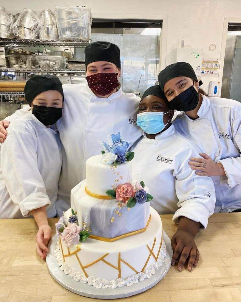 Four Escoffier students posing with a decorated cake in a kitchen