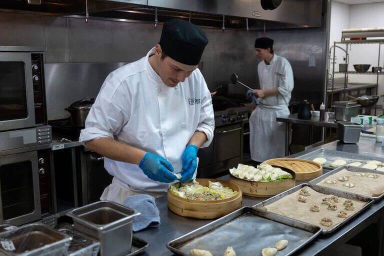 Student wearing a uniform and blue gloves preparing dumplings in a kitchen