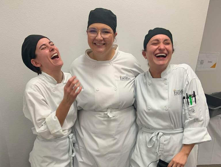 Three Escoffier students laughing as they pose for a photo while in uniform