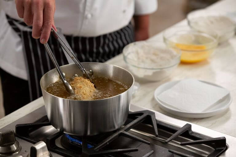 Chef removing fried chicken with tongs from boiling hot oil