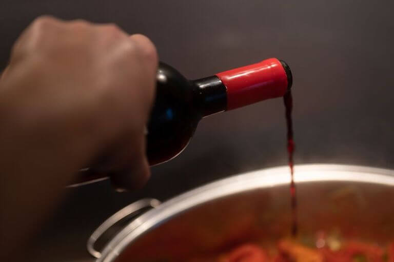 Chef pouring red wine from a bottle into a pot