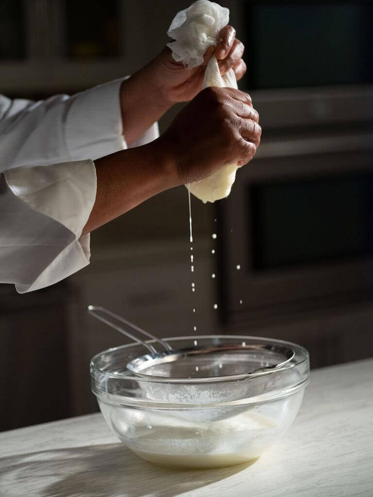 Close up of hands draining fresh cheese through cheesecloth