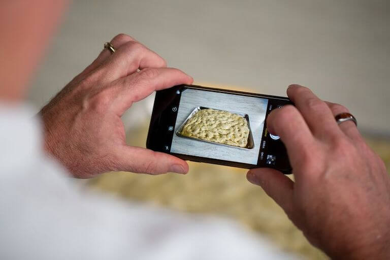 Close up of hands taking a photo of Focaccia Bread with a phone