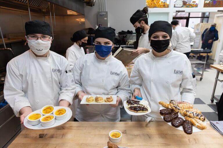 Escoffier boulder students holding their finished desserts on white plates for a photo