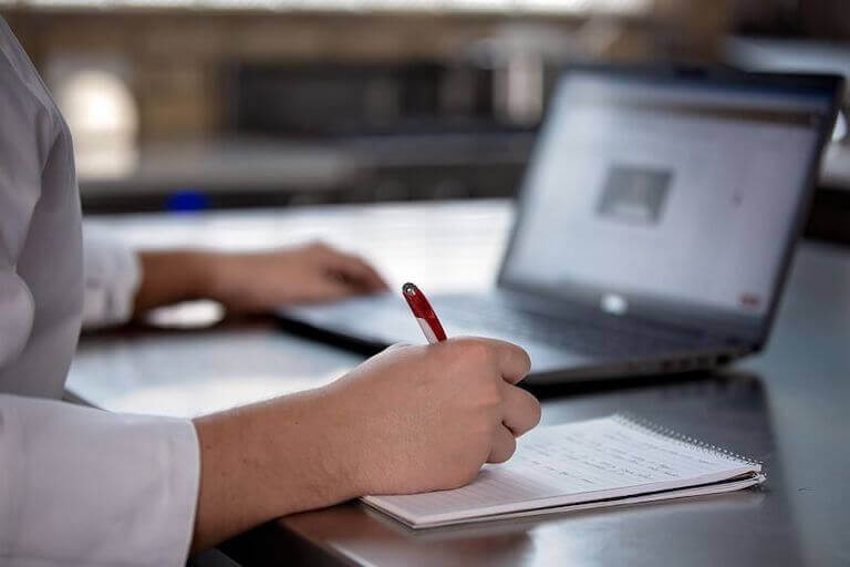 Close up a writer writing notes while using a laptop