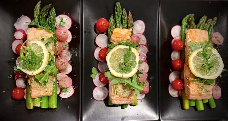 Three plates of salmon with lemon slices on black rectangle plates