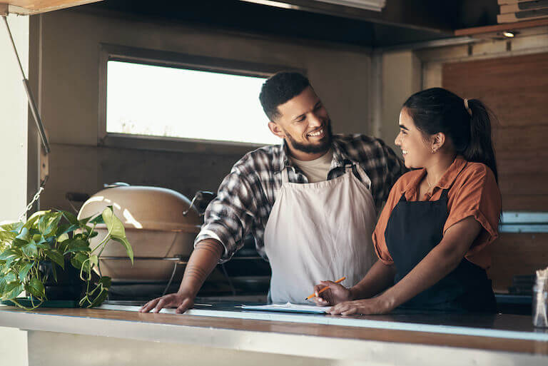 Two restaurant employees are talking at a counter with aprons on