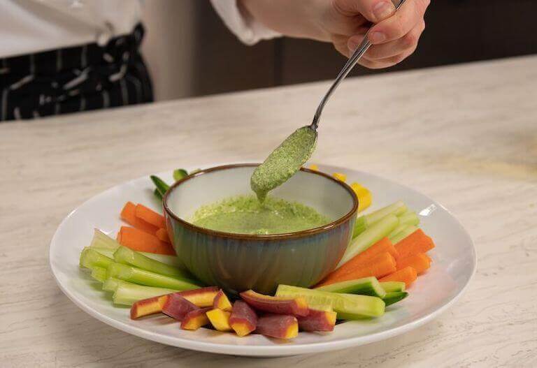 A raw crudite plate with green goddess dressing in a green bowl