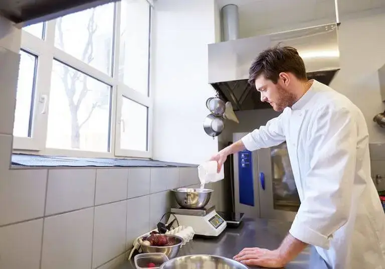 Chef pouring flour into mixing bowl on scale.