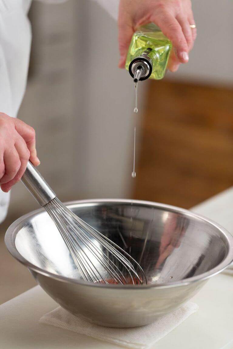 Chef pouring oil from a glass bottle into a metal bowl