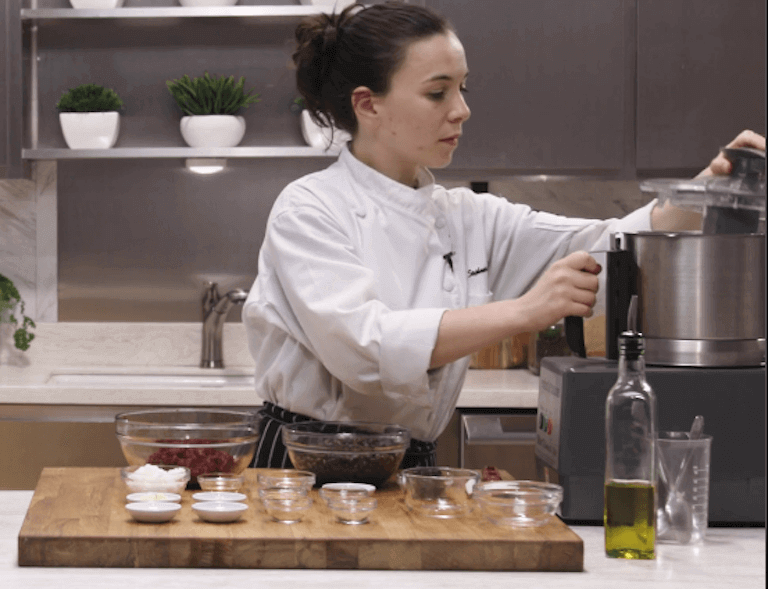 Chef standing in kitchen with ingredients laid out in front of them as they open a pressure cooker