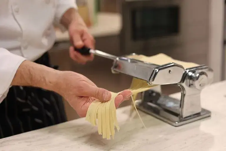 Closeup of a pair of hands guiding fresh pasta as it comes through a pasta machine.