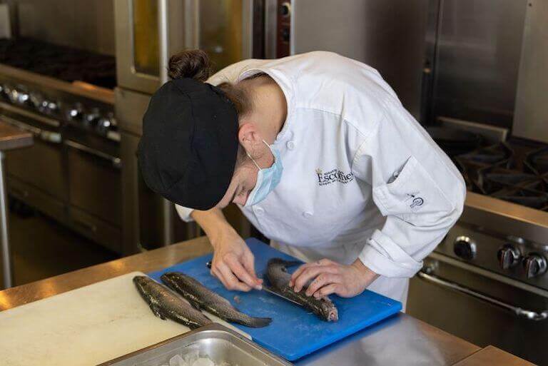 Escoffier student cutting a fish on a blue cutting board