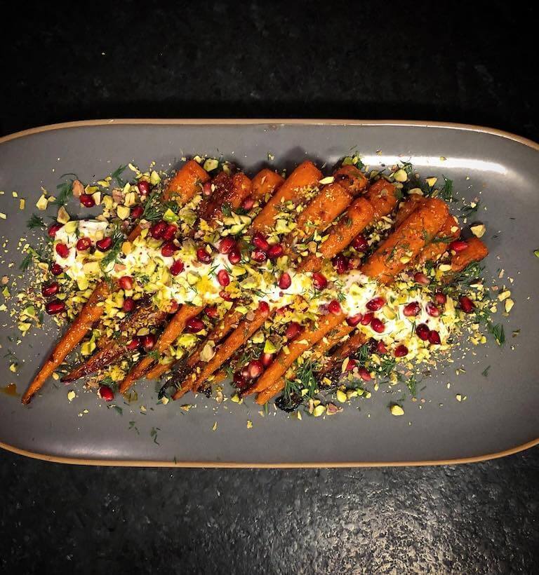 carrots and pomegranate seeds plated on a dark grey tray