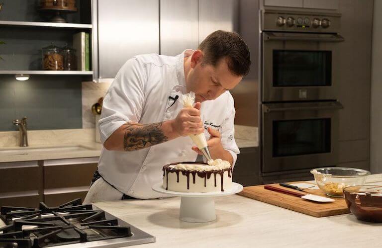 Chef decorating a vanilla cake with brown and white icing
