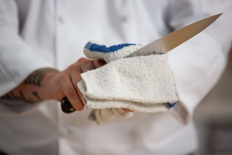 Chef knife being sanitized with a blue and white towel