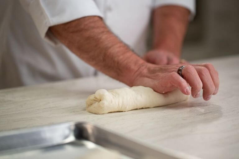 Chefs hands shaping dough for a baguette