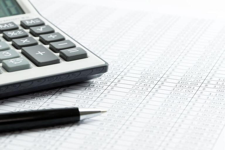 Close up photo of a calculator and pen sitting on a financial report 