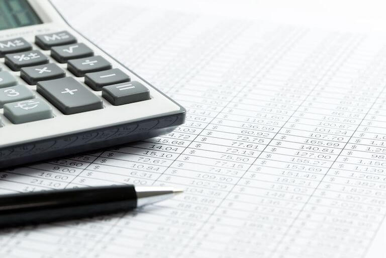 Close up photo of a calculator and pen sitting on a financial report