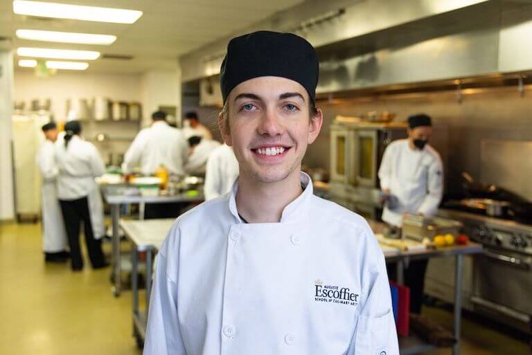 Escoffier student wearing their uniform in a kitchen smiling and posing for a photo