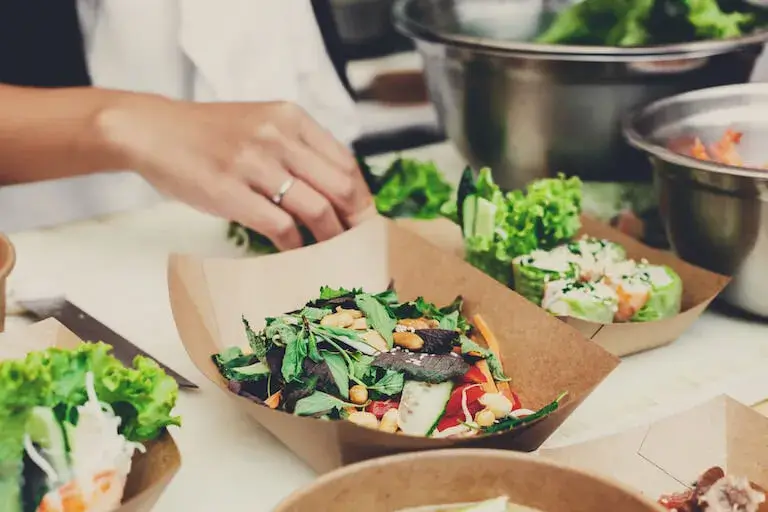 Hands assembling a fresh, plant-based meal, representing culinary entrepreneurship in meal prep, catering, or health-focused food services.