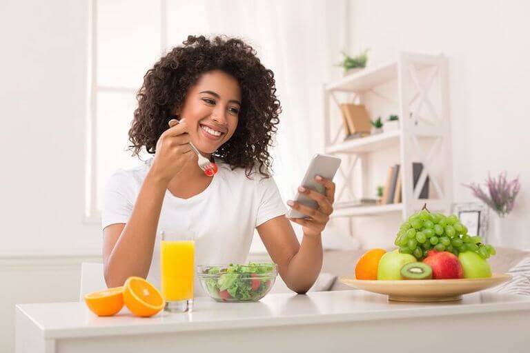 Woman smiling at her phonr while she eats a salad and orange juice