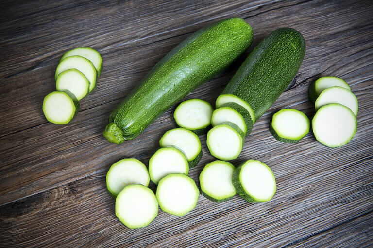 A full zucchini next to zucchini slices on a wood table