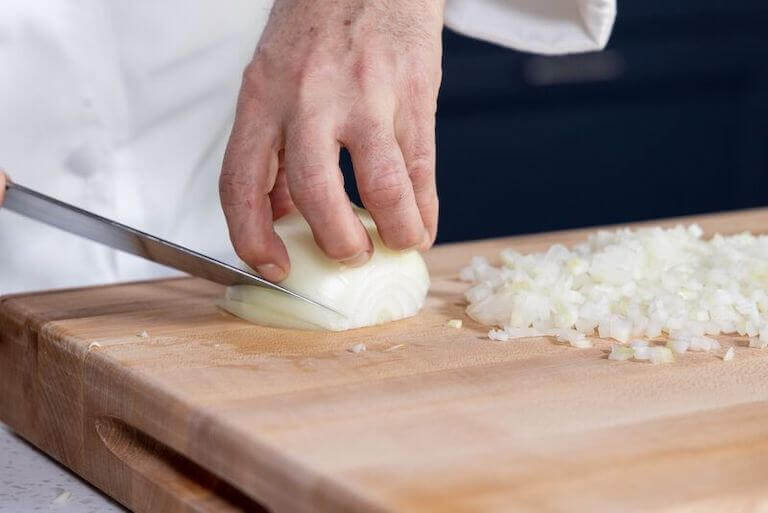 A pair of hands performing a lyonnaise cut on an onion