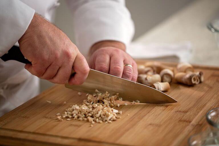 A closeup view of a pair of hands mincing mushrooms on a wooden cutting board.