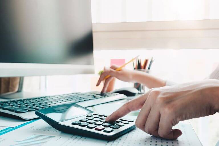 Close up photo of a hand typing on a calculator while the other hand holds a pencil