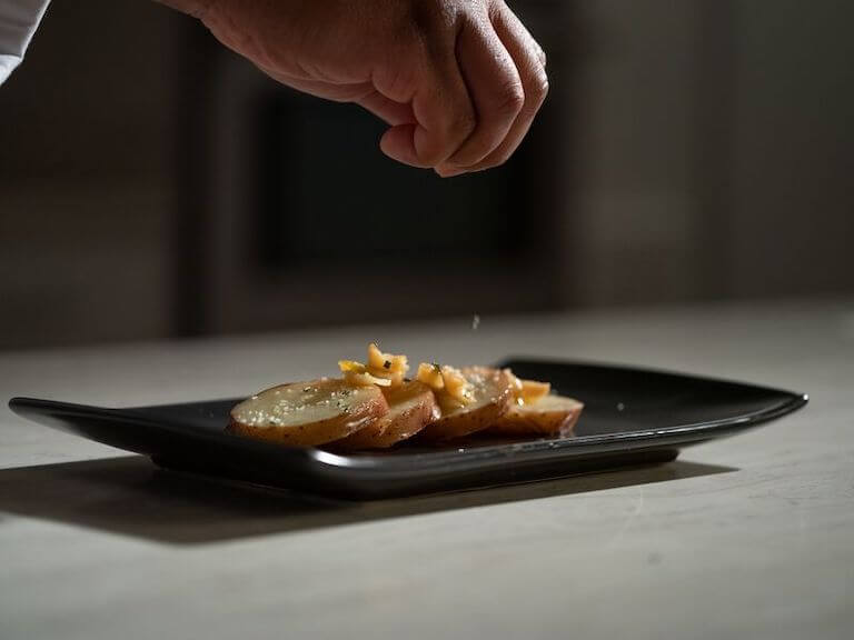 Hand sprinkling salt onto plated potatoes confit