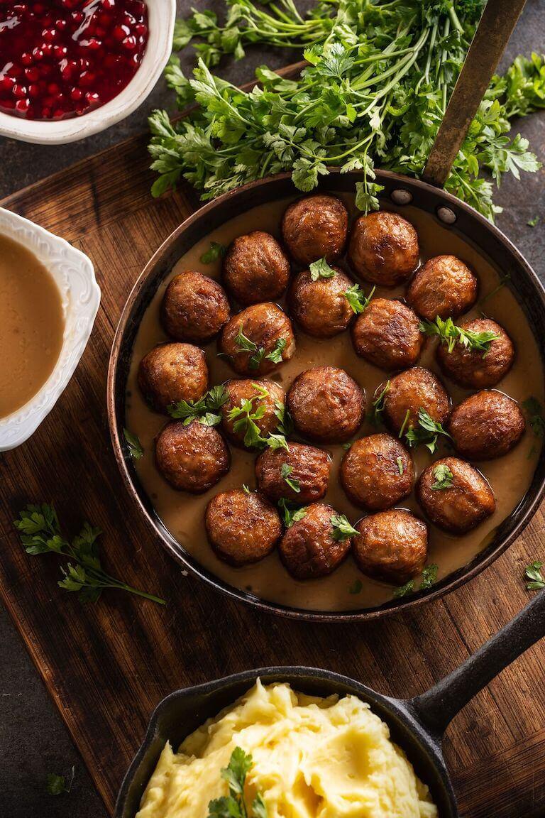 Meatballs and sauce in a pan next to mashed potatoes and cranberry sauce