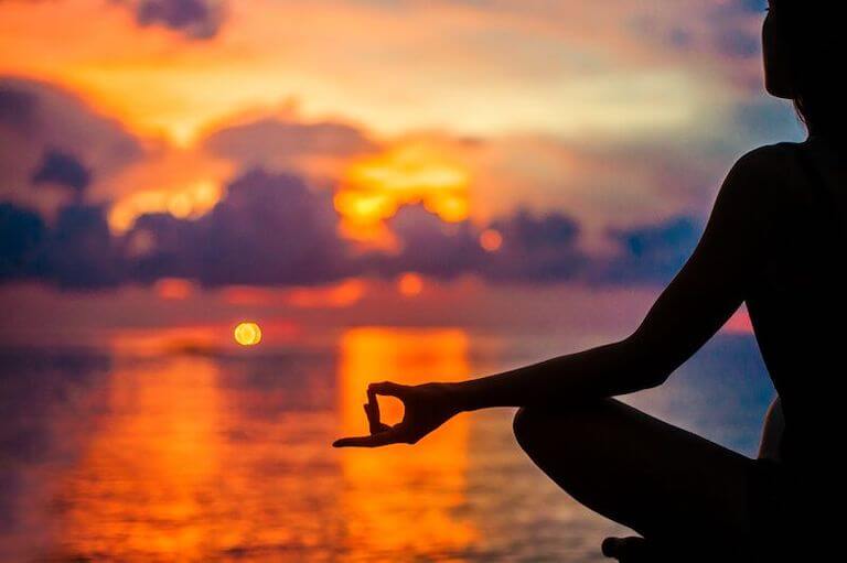 Person meditating in front of a lake during sunset