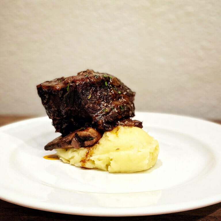 Red-Wine Braised Beef Short Rib with Roasted Garlic Rosemary Mashed Potatoes on a white plate