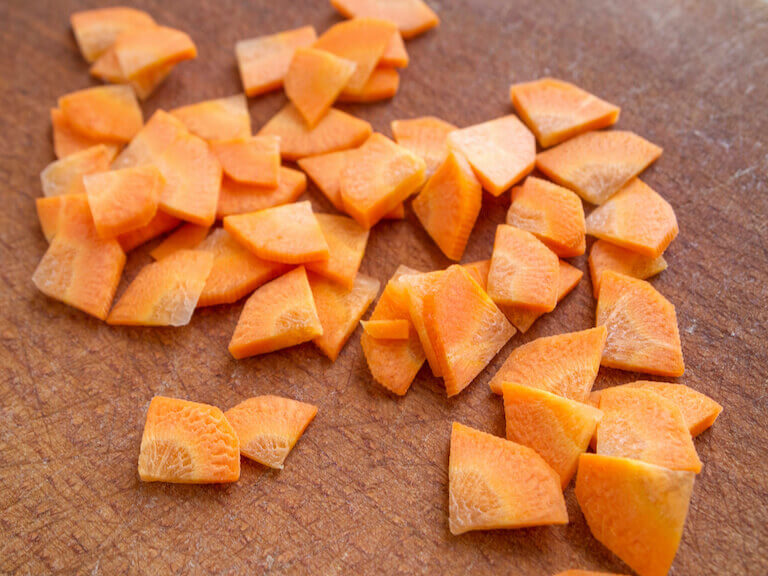 Side view of sliced carrots on a brown wooden cutting board