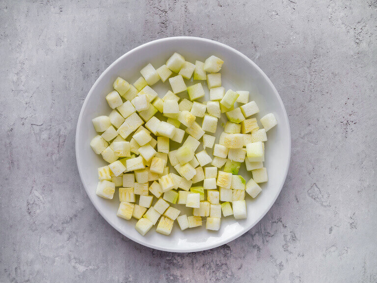 An overhead view of chopped zucchini on a white plate.