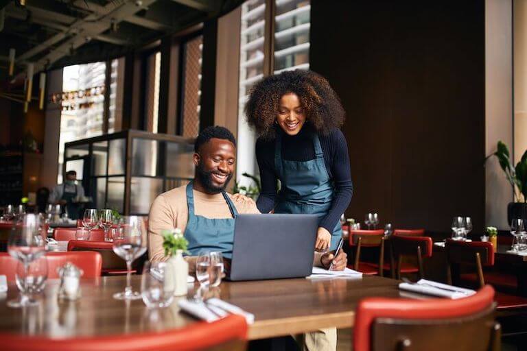 Two restaurant employees in aprons looking at a laptop