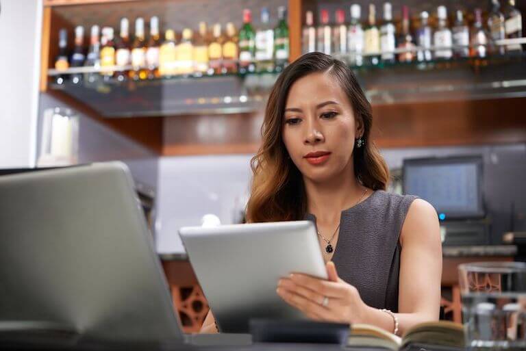 Person dressed in a grey shirt standing in front of a bar looking at a tablet