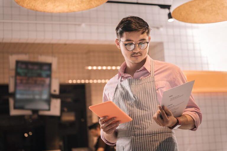 Person wearing glasses and a striped apron reviewing a menu