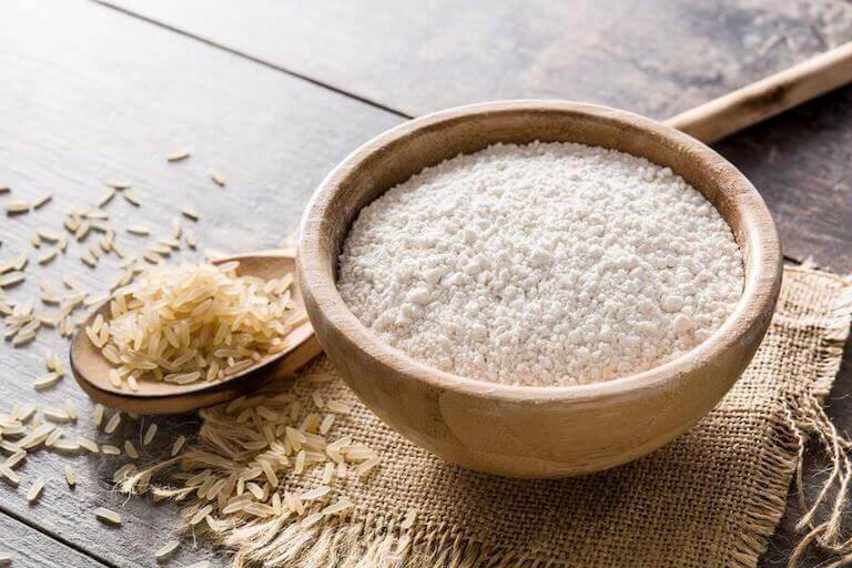 Rice flour in a wood. bowl next to a spoonful of rice