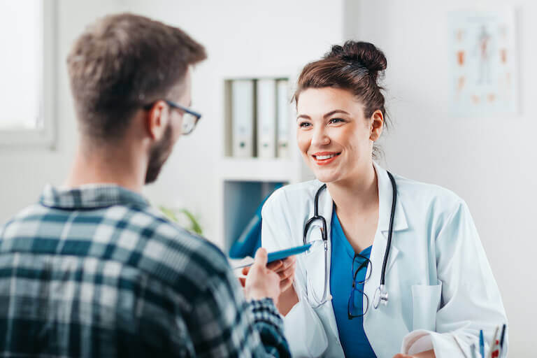 Smiling doctor in a white coat handing a piece of paper to a patient