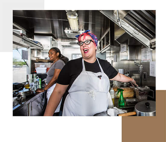 A woman with pink hair and a bandana talking inside of her food truck