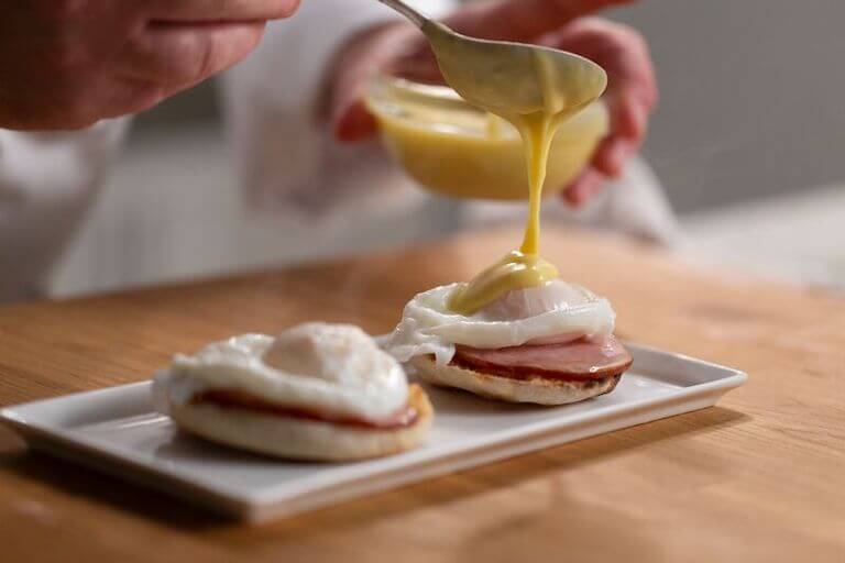 Chef adding Hollandaise Sauce to Eggs Benedict