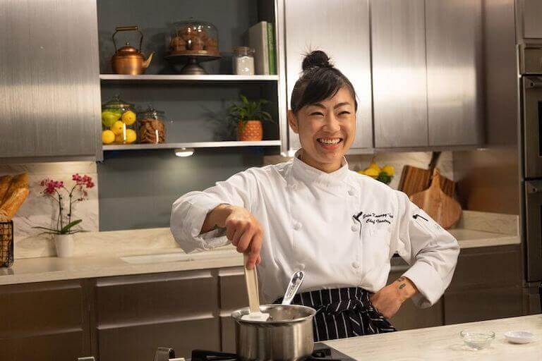 Chef smiling and stirring sauce in a metal pot on the stove