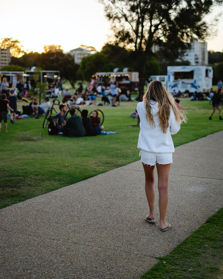 Customer wearing white walking towards and open park with food trucks lined up next to the grass